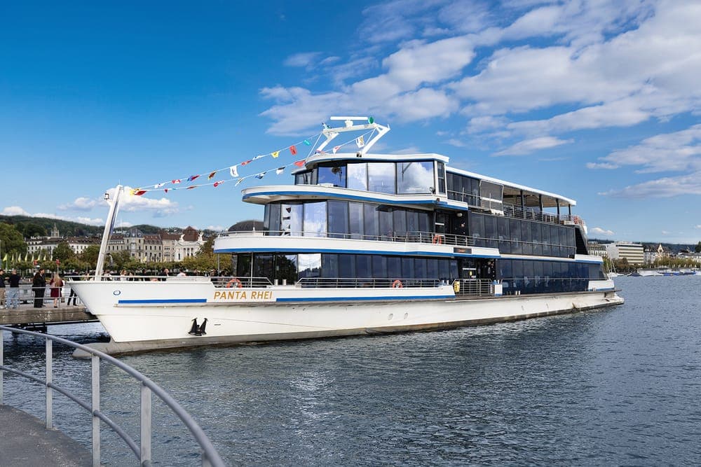 The Panta Rhei boat at the pier under a blue sky, flags strung from its mast