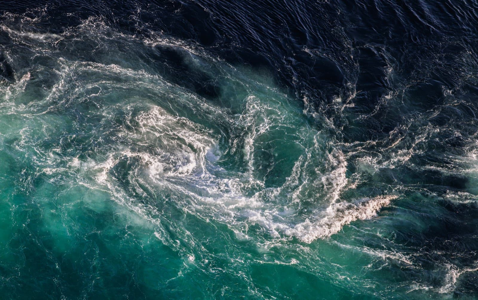 Aerial view of two currents meeting, dark blue water folding into turquoise