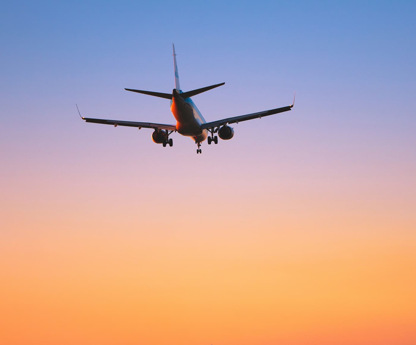 An airliner on approach at dusk, silhouetted against a sky running from blue to orange